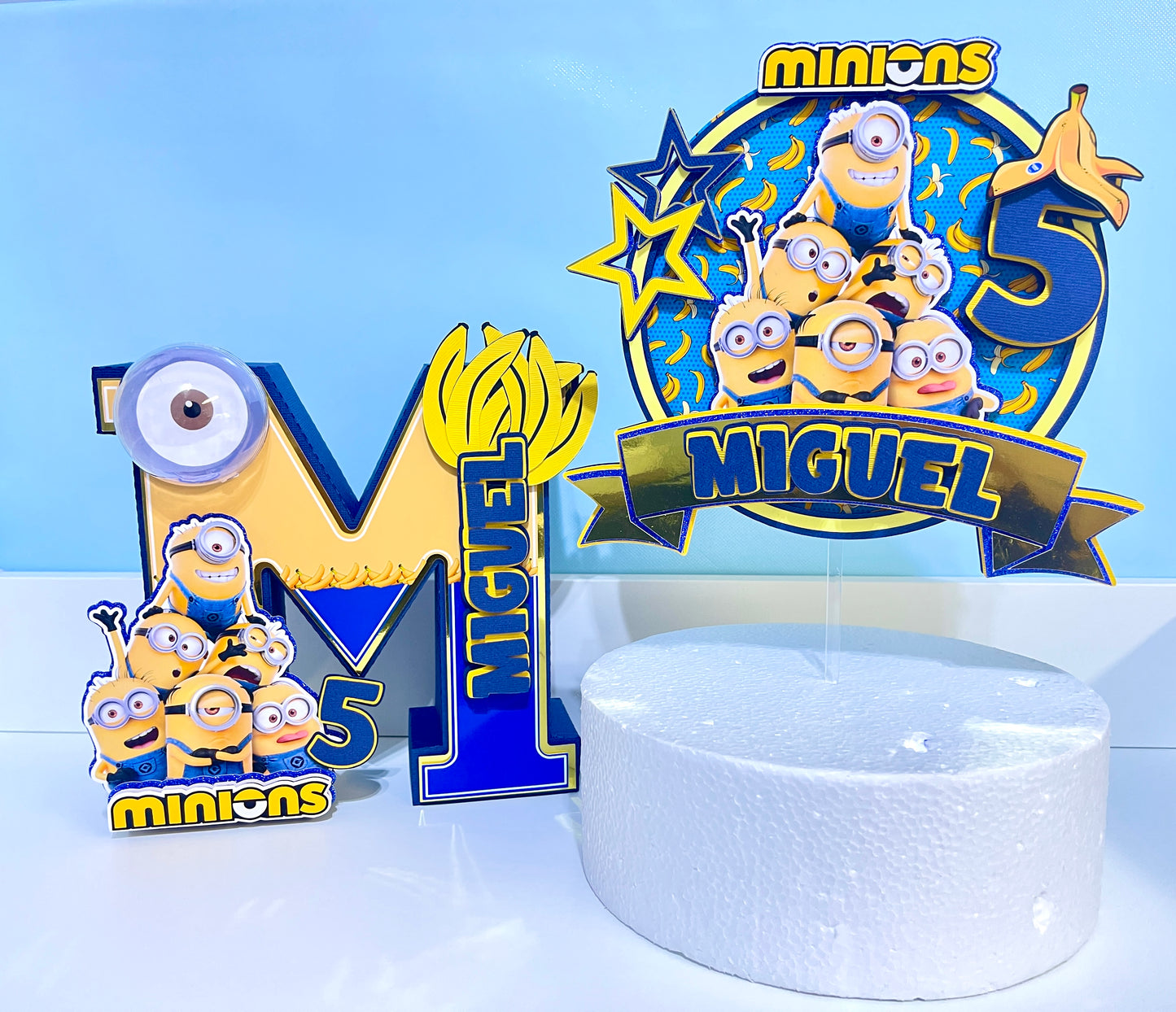 Custom Minions-themed cake topper featuring vibrant colors and intricate designs, perfect for adding a fun touch to birthday celebrations. Made from high-quality cardstock and carefully hand-assembled for precision and detail.