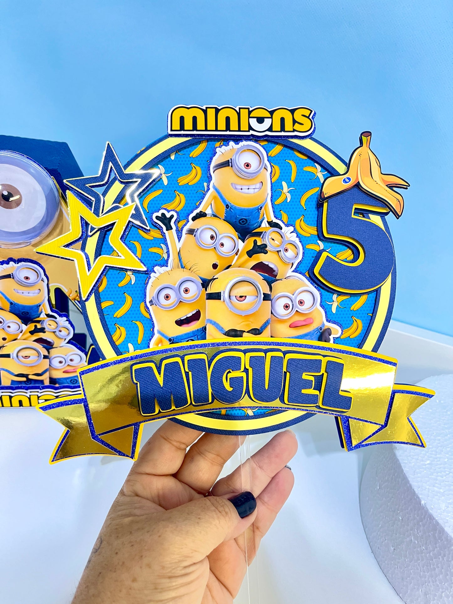 Custom Minions-themed cake topper featuring vibrant colors and intricate designs, perfect for adding a fun touch to birthday celebrations. Made from high-quality cardstock and carefully hand-assembled for precision and detail.