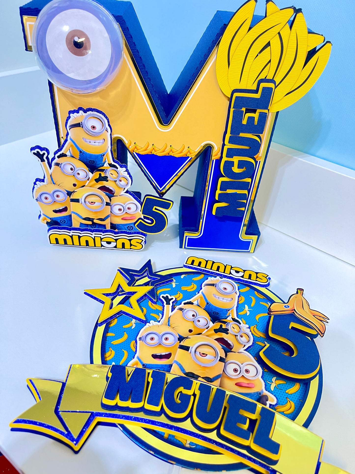 Custom Minions-themed cake topper featuring vibrant colors and intricate designs, perfect for adding a fun touch to birthday celebrations. Made from high-quality cardstock and carefully hand-assembled for precision and detail.