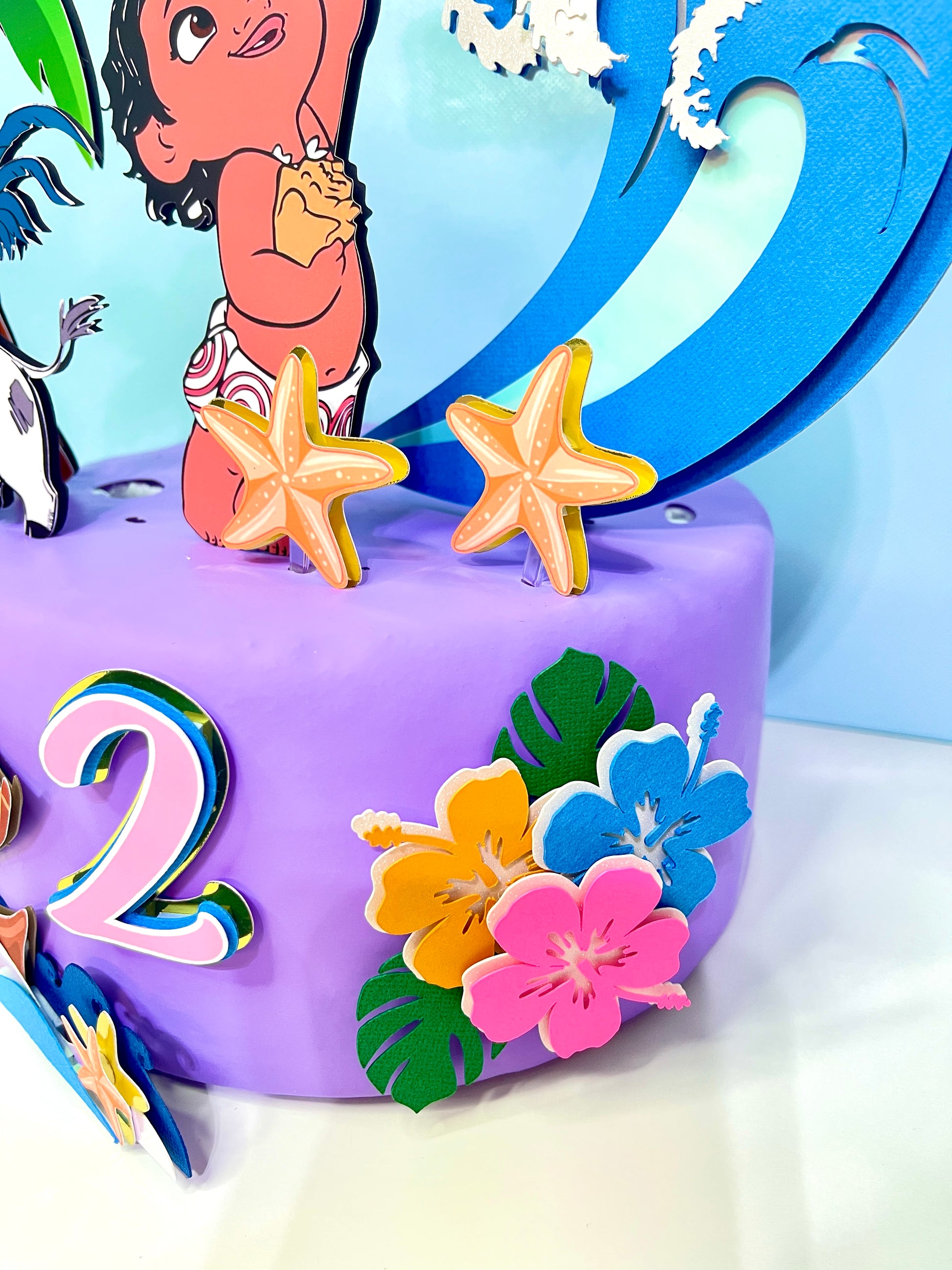 Baby Moana cake topper featuring an adorable Baby Moana figurine surrounded by tropical flowers and ocean-themed decorations.