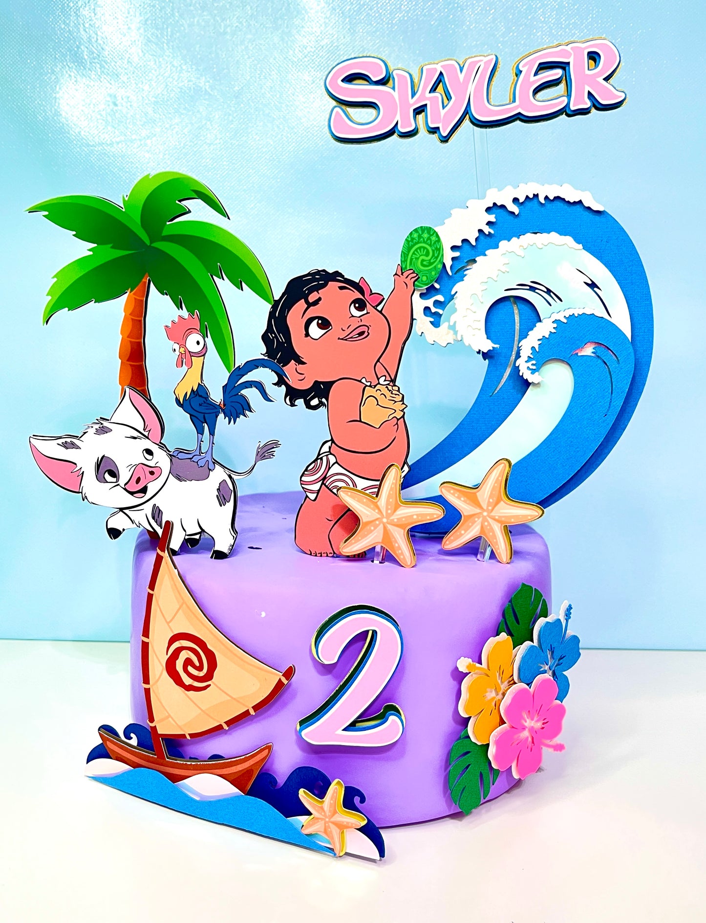 Baby Moana cake topper featuring an adorable Baby Moana figurine surrounded by tropical flowers and ocean-themed decorations.